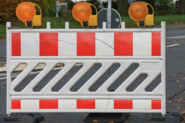 Zdjęcie przedstawia biało-czerwoną tymczasową barierę drogową. Na barierze znajdują się żółte sygnalizatory świetlne.
