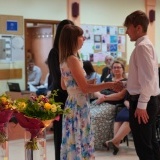 Zakończenie roku szkolnego w Zespole Szkół nr 2 we Wronkach, na pierwszym planie bukiety kwiatów, na drugim nauczycielka gratuluje osiągnięć uczniowi 