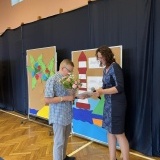 Uczeń wręcza kwiaty dyrektor Szkół Specjalnych w Szamotułach Natalii Sobczak, w tle czarna kotara i kolorowe, wakacyjne makiety 