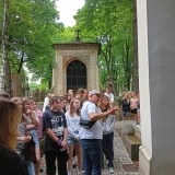 Uczniowie na Powązkach słuchają przewodnika. W tle widoczne mauzoleum  i drzewa 